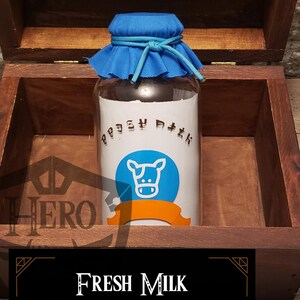 May include: A glass bottle of "Fresh Milk" with a blue cloth top, inside a wooden box. The bottle has a white label with a cow graphic and text. The box is open, revealing the bottle. Text on the label says "Sweet and refreshing milk of the highest quality."