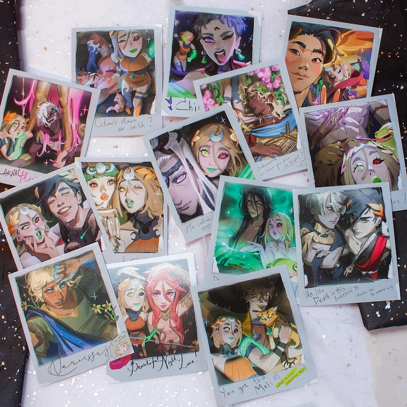 May include: A collection of artistic polaroid-style prints featuring colorful illustrations of characters with various expressions and styles. Some prints include handwritten text like "Rita's stain or sonth?" and "You got this Meli!"