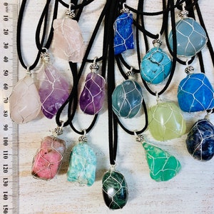 May include: Assortment of 14 colorful gemstone pendants with wire cages, each on a black cord necklace. The stones include amethyst, rose quartz, aquamarine, turquoise, green aventurine, and more.