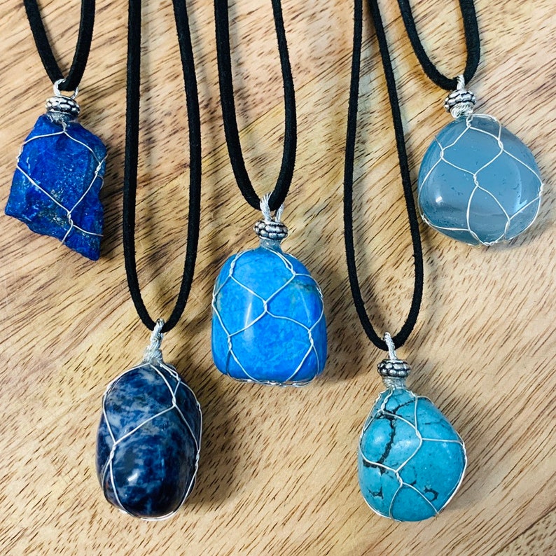 May include: Five necklaces with blue and grey stones wrapped in silver wire mesh. The necklaces are on a wooden surface and have black cords.