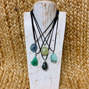 May include: Five necklaces with different colored stones wrapped in wire. The stones are green, blue, and light green. The necklaces are on a white mannequin bust.