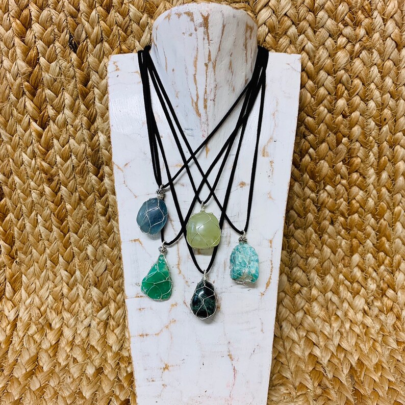 May include: Five necklaces with different colored stones wrapped in wire. The stones are green, blue, and light green. The necklaces are on a white mannequin bust.