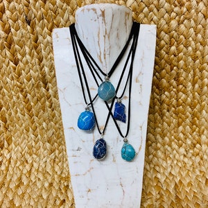 May include: Five necklaces with different blue and turquoise stones wrapped in silver wire. The necklaces are on a white mannequin and have black cords.