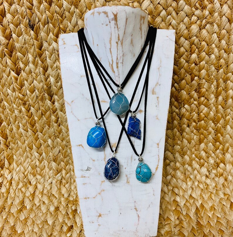 May include: Five necklaces with different blue and turquoise stones wrapped in silver wire. The necklaces are on a white mannequin and have black cords.