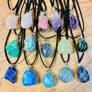 May include: A collection of 14 wire-wrapped crystal pendants on black suede cords. The crystals are various shapes and colors, including amethyst, rose quartz, green aventurine, and blue lapis lazuli.
