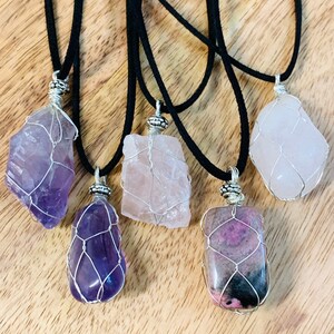 May include: Five wire-wrapped crystal pendants on black cords. The crystals are amethyst, rose quartz, and pink and black rhodochrosite.