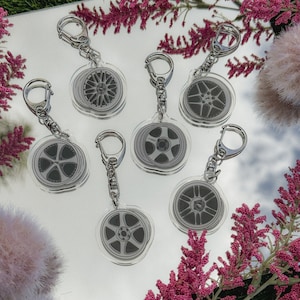 May include: Seven silver keyrings with clear acrylic charms featuring black and white images of car wheels. The charms are attached to silver chains with silver lobster clasps.
