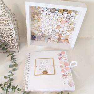 May include: A white spiral bound guest book with a pink and gold honeycomb design on the cover. The book has a tag that says "To the New Mr & Mrs A New Chapter Celebrate Your Wedding Day".