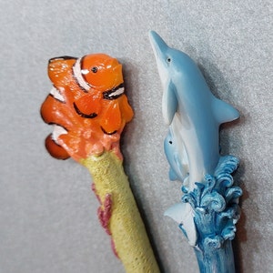 Nautische Ozeanstifte - Blaue Delfine oder Clownfische Amphiprioninae - 2 Stile zur Auswahl - Handgefertigt aus Harz, geschnitzten und bemalten Naturstiften