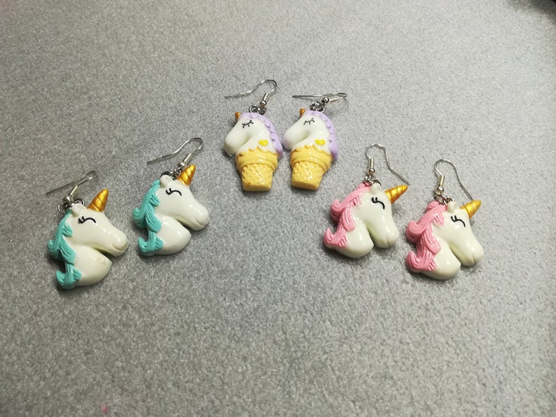 K&ouml;nnte beinhalten: Ein Set mit sechs Ohrringen zum Thema Einhorn. Zwei Paare zeigen einen Einhornkopf mit einer blauen M&auml;hne und einem Horn, zwei Paare zeigen einen Einhornkopf mit einer rosa M&auml;hne und einem Horn und zwei Paare zeigen einen Einhornkopf mit einer lila M&auml;hne und einem Horn.