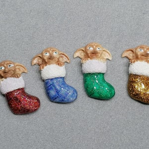 May include: Four Christmas stocking ornaments featuring a brown elf character with large ears and a white fur trim. The stockings are decorated with glitter in red, blue, green, and gold.