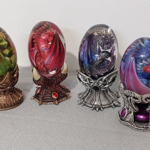 May include: Four dragon figurines are encased in glass orbs and placed on decorative stands. The dragons are in various colors, including green, red, purple, and blue.