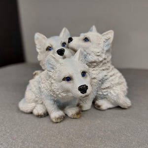 May include: Three white ceramic wolf figurines with blue eyes. The wolves are huddled together in a playful pose.