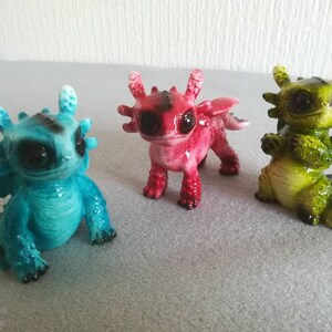 May include: Three small dragon figurines, one blue, one red, and one green. The dragons have large eyes and are in a sitting position.