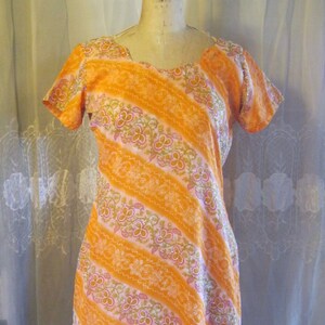 May include: A short-sleeved orange and white dress with a floral pattern. The dress has a scoop neckline and a straight silhouette.