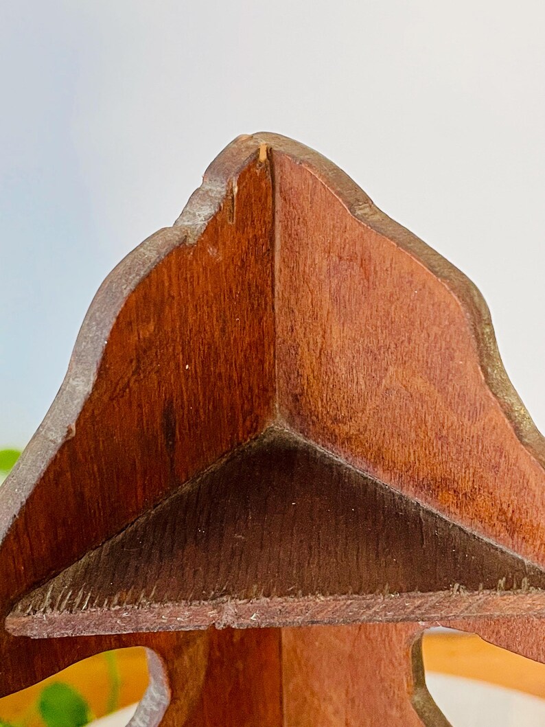 K&ouml;nnte beinhalten: Nahaufnahme eines dekorativen Holzobjekts mit dreieckiger Form. Das Holz hat eine rotbraune Farbe mit sichtbarer Maserung. Die Kanten sind leicht abgerundet und haben einen helleren Ton.