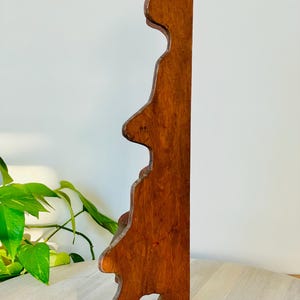 K&ouml;nnte beinhalten: Ein Vintage-Wandregal aus Holz mit warmem, r&ouml;tlich-braunem Finish. Das Regal hat eine dekorative, gewellte Kante und ein einzigartiges, asymmetrisches Design. Das Regal ist aus massivem Holz gefertigt und scheint in gutem Zustand zu sein.