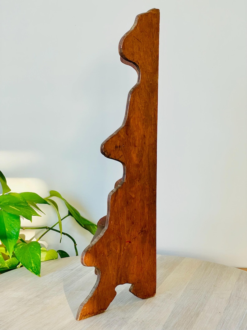 K&ouml;nnte beinhalten: Ein Vintage-Wandregal aus Holz mit warmem, r&ouml;tlich-braunem Finish. Das Regal hat eine dekorative, gewellte Kante und ein einzigartiges, asymmetrisches Design. Das Regal ist aus massivem Holz gefertigt und scheint in gutem Zustand zu sein.