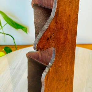 K&ouml;nnte beinhalten: Ein zweistufiges Holzregal mit r&ouml;tlich-braunem Finish. Das Regal hat ein einzigartiges, geschwungenes Design an den Kanten und scheint aus massivem Holz gefertigt zu sein. Die Regale sind offen und bereit, Gegenst&auml;nde auszustellen.