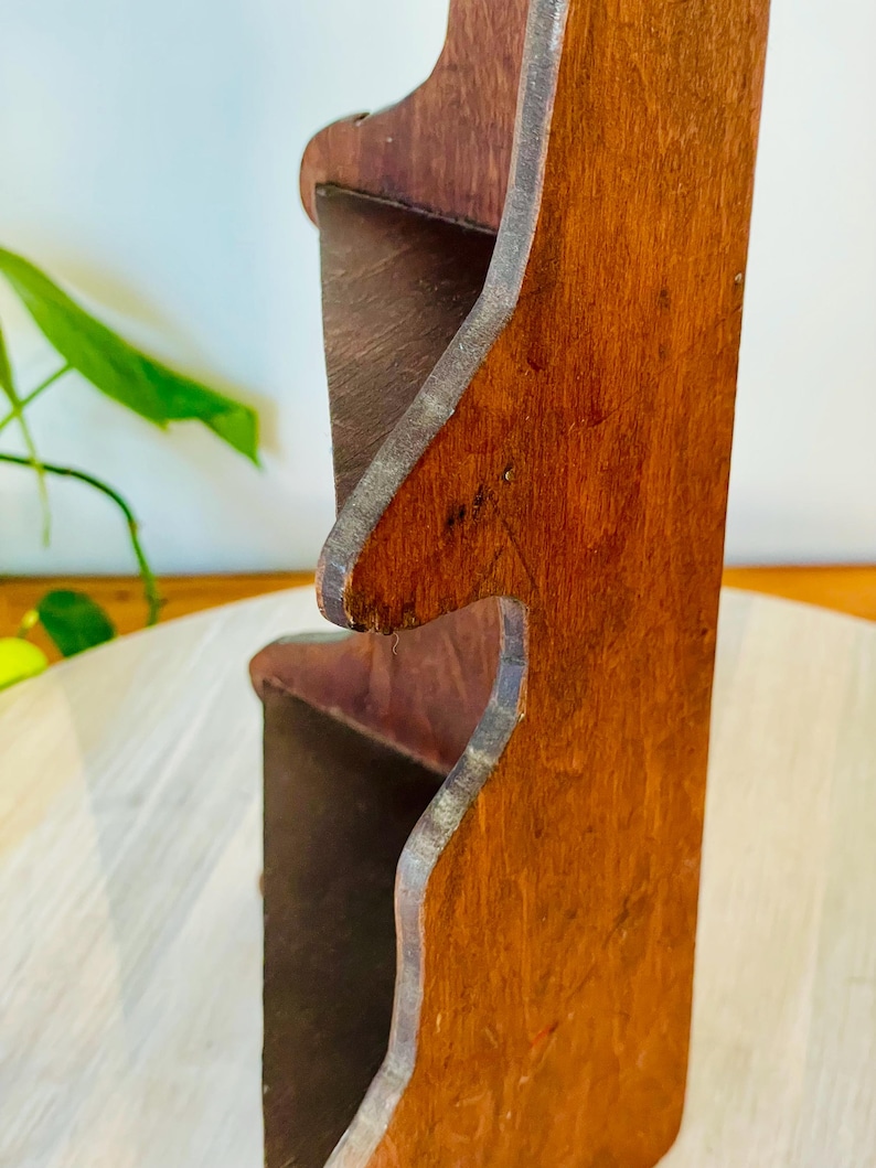 K&ouml;nnte beinhalten: Ein zweistufiges Holzregal mit r&ouml;tlich-braunem Finish. Das Regal hat ein einzigartiges, geschwungenes Design an den Kanten und scheint aus massivem Holz gefertigt zu sein. Die Regale sind offen und bereit, Gegenst&auml;nde auszustellen.