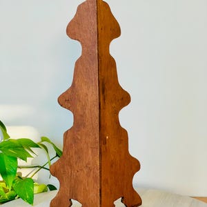 K&ouml;nnte beinhalten: Ein Vintage-Ausstellungsst&auml;nder aus Holz mit warmbraunem Finish. Der St&auml;nder hat ein einzigartiges, symmetrisches Design mit mehreren Ebenen und einer dekorativen Oberseite. Er wird wahrscheinlich zum Ausstellen von Gegenst&auml;nden verwendet.
