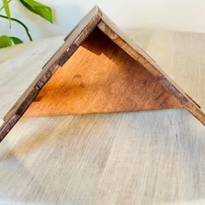 K&ouml;nnte beinhalten: Ein dreieckiges Regal aus Holz mit nat&uuml;rlicher Holzoberfl&auml;che. Das Regal hat ein schr&auml;ges Design und besteht aus mehreren Holzst&uuml;cken, die miteinander verbunden sind. Das Regal wird auf einer hellen Oberfl&auml;che pr&auml;sentiert.