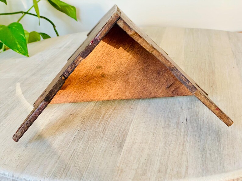 K&ouml;nnte beinhalten: Ein dreieckiges Regal aus Holz mit nat&uuml;rlicher Holzoberfl&auml;che. Das Regal hat ein schr&auml;ges Design und besteht aus mehreren Holzst&uuml;cken, die miteinander verbunden sind. Das Regal wird auf einer hellen Oberfl&auml;che pr&auml;sentiert.
