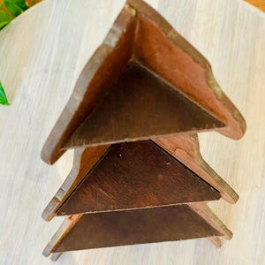 K&ouml;nnte beinhalten: Ein Weinregal aus Holz mit dreieckigem Design. Das Regal besteht aus dunkelbraunem Holz und hat drei Ebenen. Die Kanten des Regals sind hellbraun.