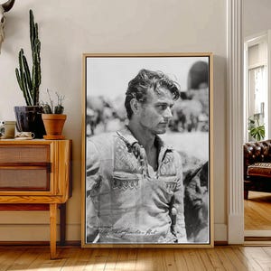May include: Black and white framed print of a man in a patterned shirt. The print is in a wooden frame and features a man looking off to the side. The print is in a room with wooden floors and a wooden cabinet.