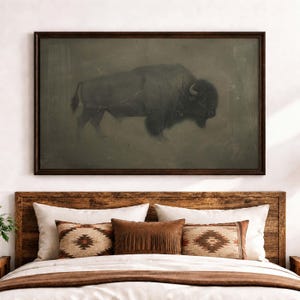 May include: A rectangular wall art piece featuring a dark, muted illustration of a bison in profile. The artwork is enclosed in a thin, dark brown wooden frame and is displayed horizontally, showcasing the animal's silhouette against a textured, earthy background.