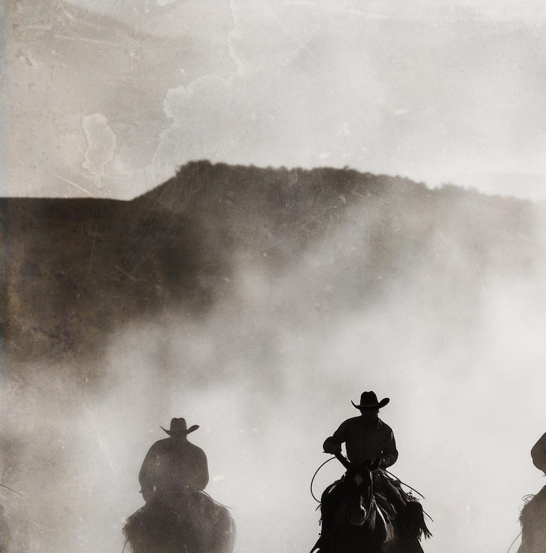 May include: Silhouettes of three cowboys riding horses through a dusty, foggy landscape. The cowboys are wearing hats and riding in a line, with the lead cowboy in the center of the image.