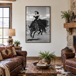 May include: A black and white framed wall art print depicting a person in a long dark gown riding a horse in a jumping motion. The image features a clear sky and a fence in the background, capturing a dynamic moment of equestrian movement.