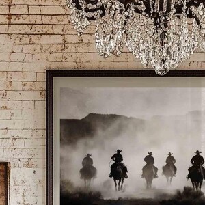 May include: Black and white photograph of five cowboys riding horses through a dusty landscape. The cowboys are silhouetted against a hazy background.