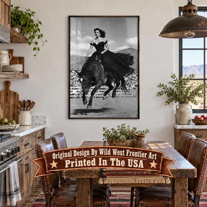 May include: A black and white framed wall art print depicting a person in a long dark gown riding a horse at a gallop. The print is displayed on a white wall above a wooden dining table. The text on the overlay reads Original Design By Wild West Frontier Art Printed In The USA.