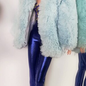 May include: A doll wearing a light blue faux fur jacket and blue metallic trousers. The doll has long black hair and is wearing silver hoop earrings.