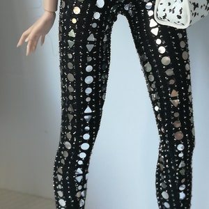 May include: Black leggings with silver sequins in a geometric pattern. The leggings are worn with a white button-down shirt and a black belt with a silver buckle.
