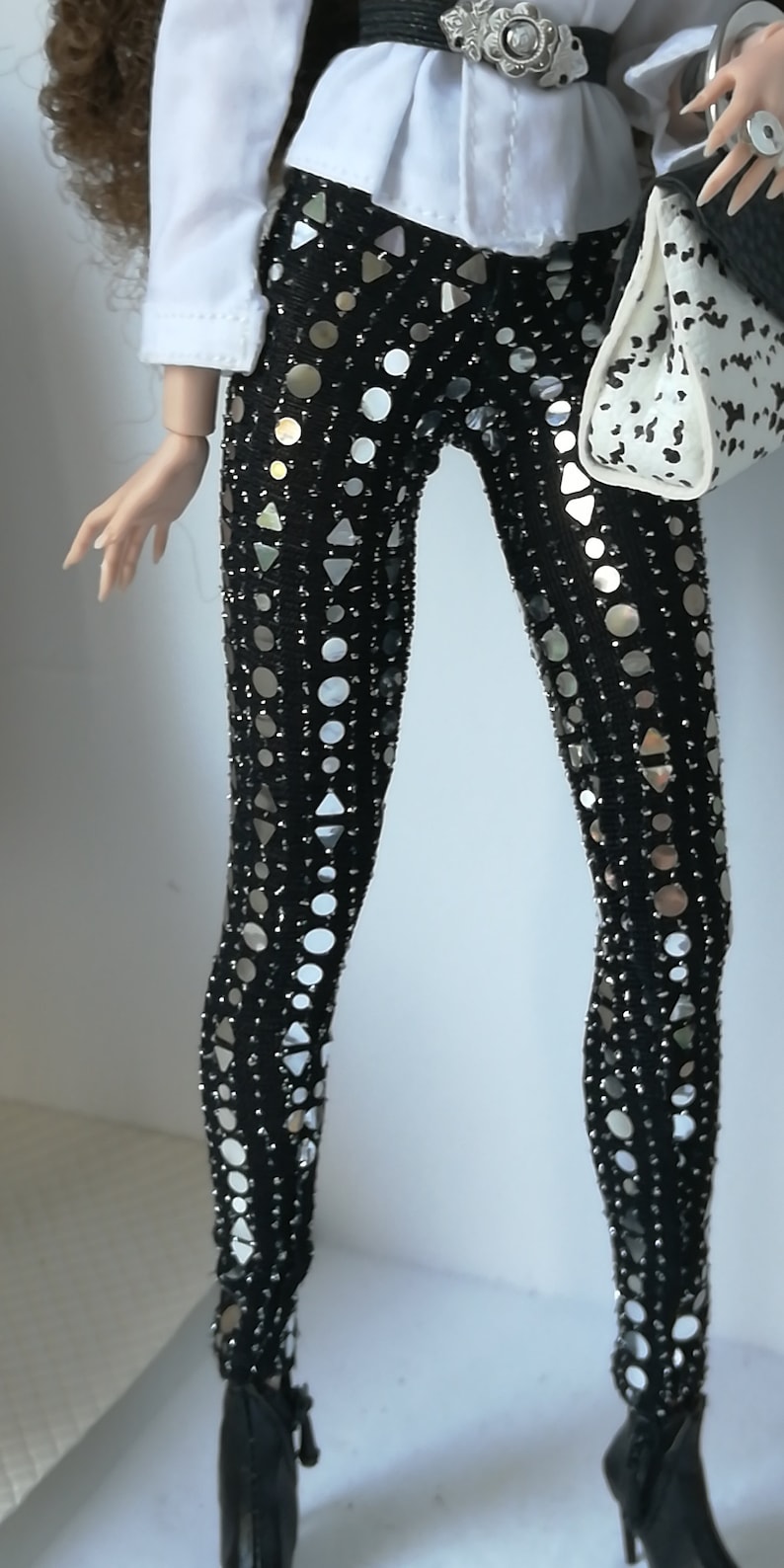 May include: Black leggings with silver sequins in a geometric pattern. The leggings are worn with a white button-down shirt and a black belt with a silver buckle.