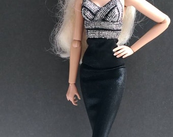 Può includere: Una bambola di moda con lunghi capelli biondi che indossa un abito nero e argento e tacchi alti neri.