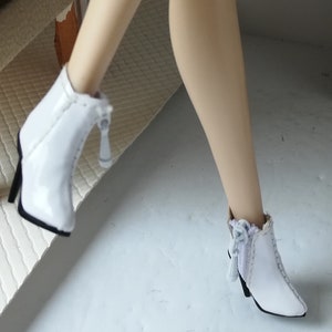May include: A pair of white ankle boots with a zipper detail and a small bow on the back. The boots have a pointed toe and a high heel.