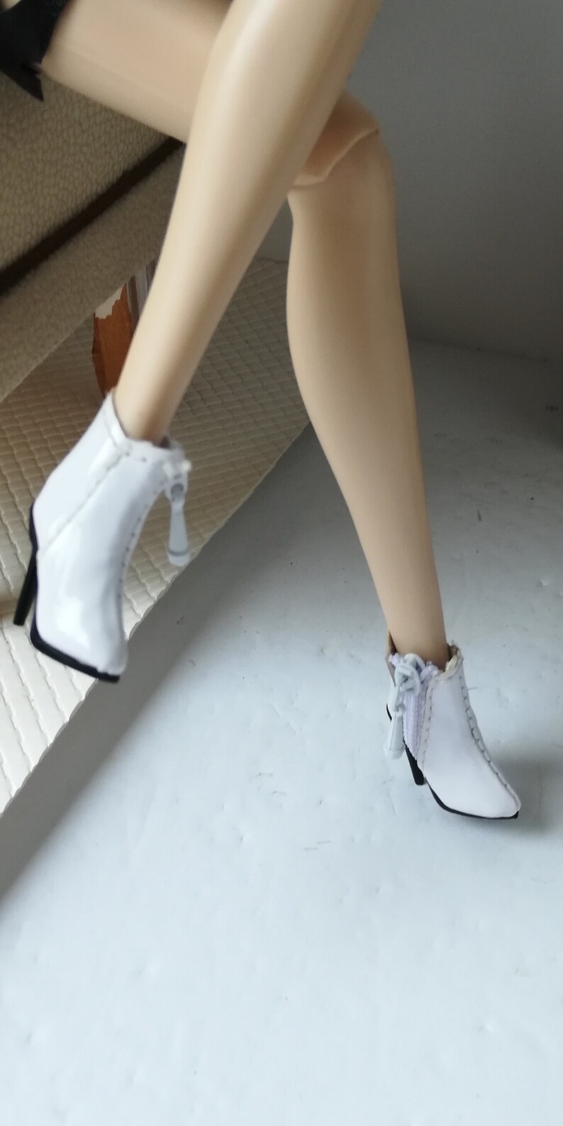 May include: A pair of white ankle boots with a zipper detail and a small bow on the back. The boots have a pointed toe and a high heel.