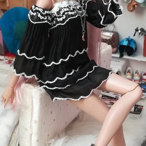 May include: A fashion doll with long pink hair wearing a black off-the-shoulder dress with white lace trim and black platform heels.