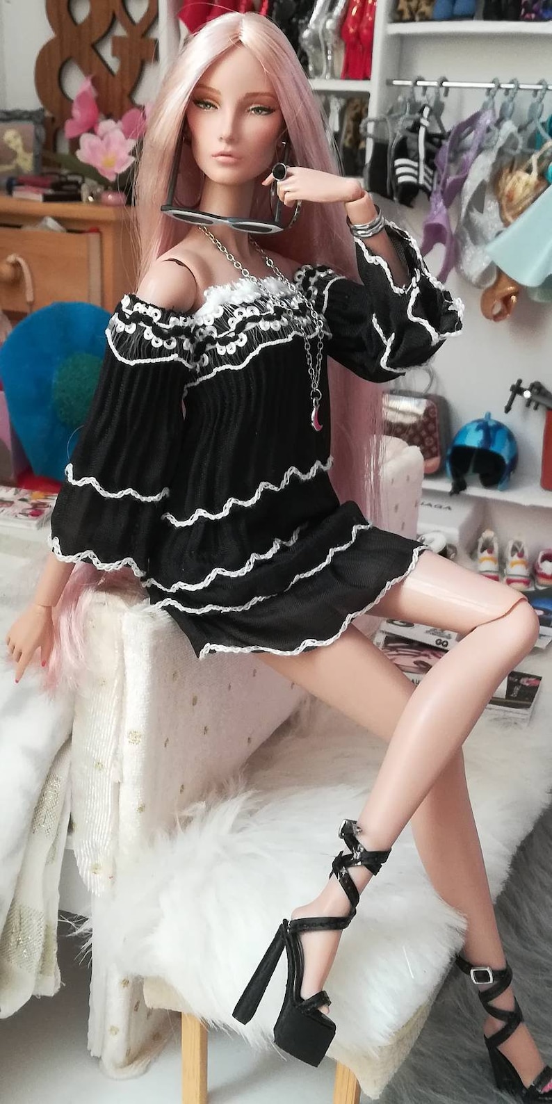 May include: A fashion doll with long pink hair wearing a black off-the-shoulder dress with white lace trim and black platform heels.