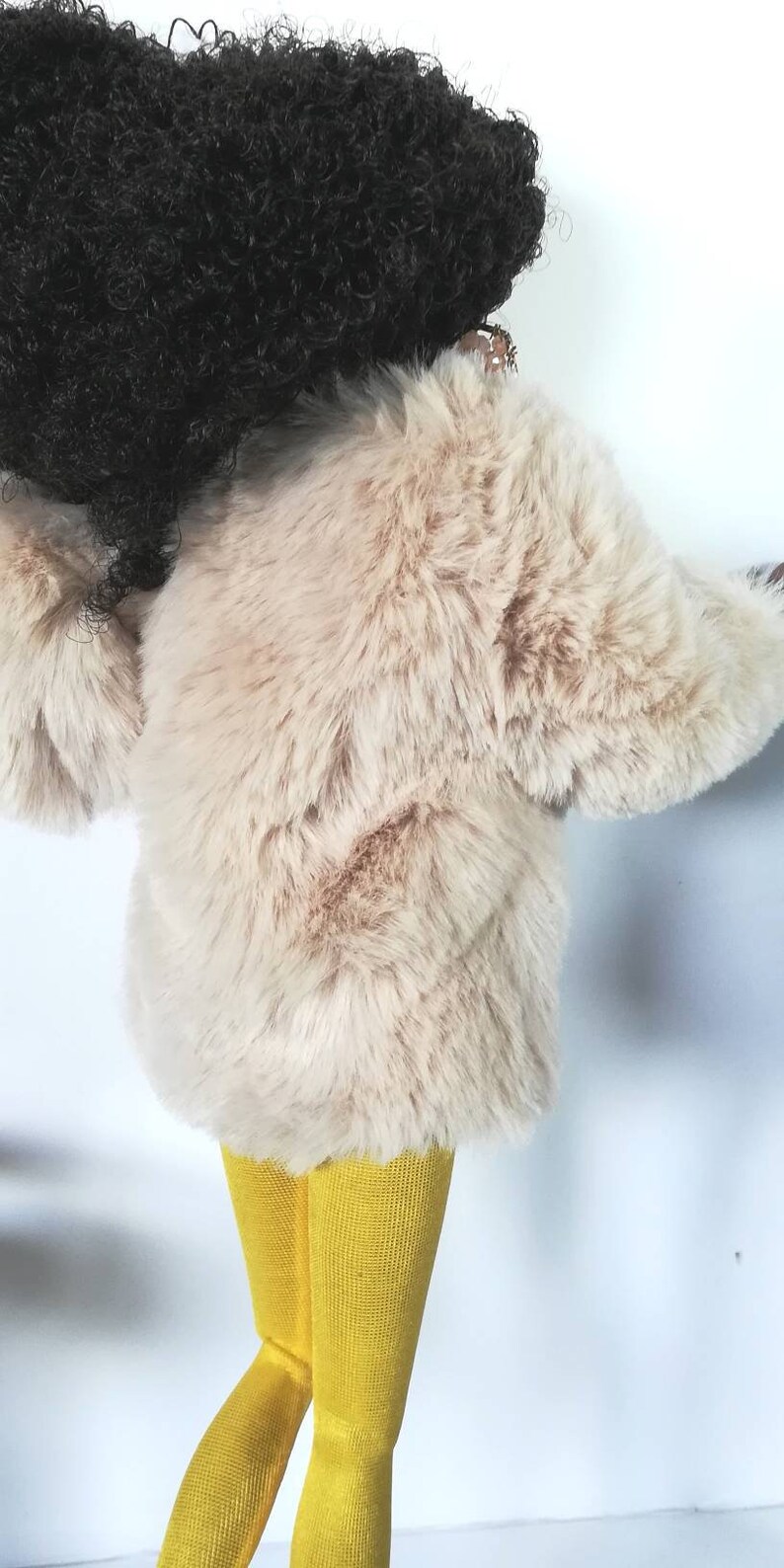 Puede incluir: Una mu&ntilde;eca con una chaqueta de piel sint&eacute;tica beige y leotardos amarillos.