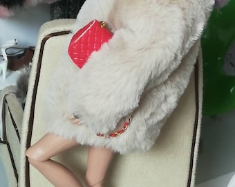 May include: A doll wearing a white faux fur coat, a red purse, and pink high heels. The doll has purple hair and is sitting on a chair.