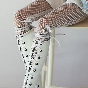 May include: White lace-up boots with a peep toe and a high heel. The boots are worn with white fishnet stockings.