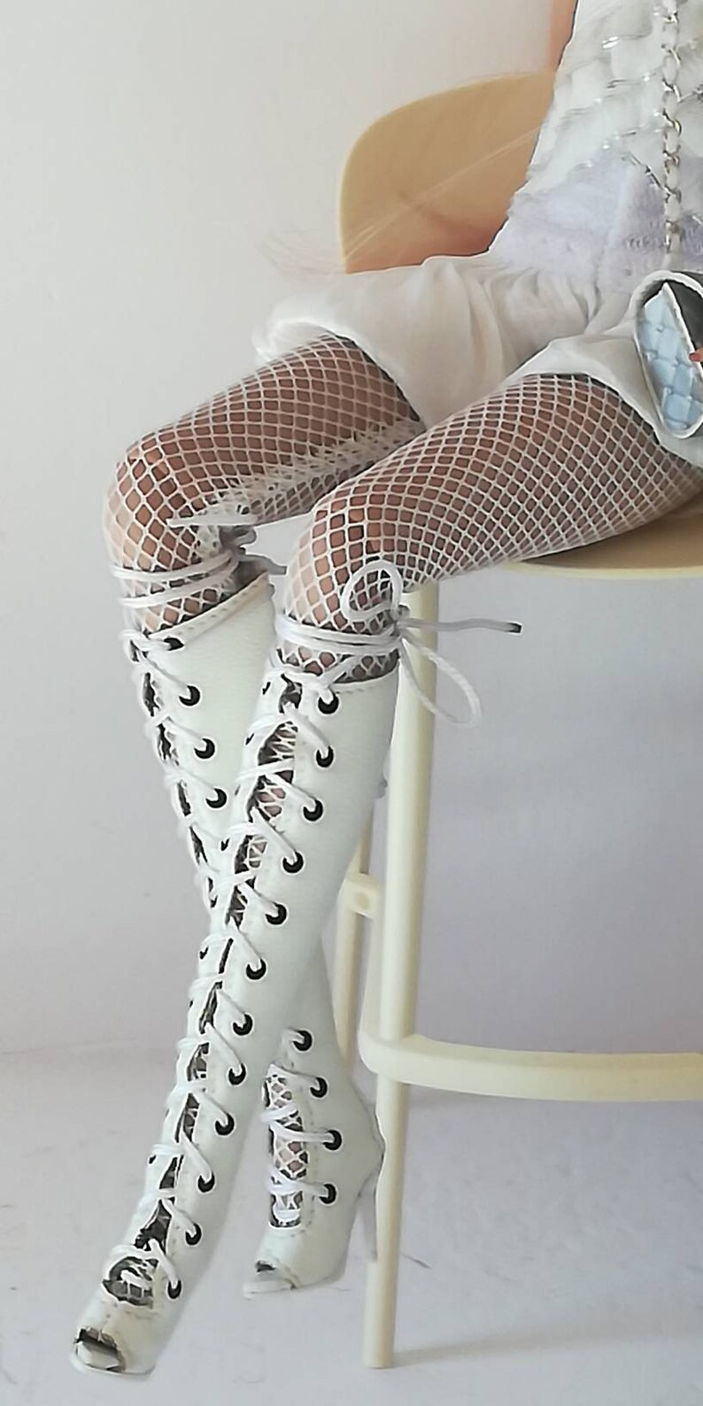 May include: White lace-up boots with a peep toe and a high heel. The boots are worn with white fishnet stockings.