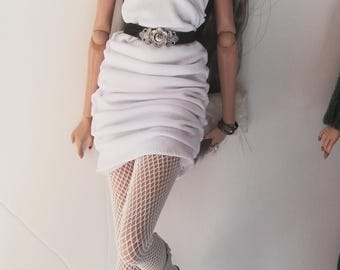 May include: A white strapless dress with a ruffled skirt and a black belt with a silver buckle. The doll is wearing white fishnet tights and silver boots.