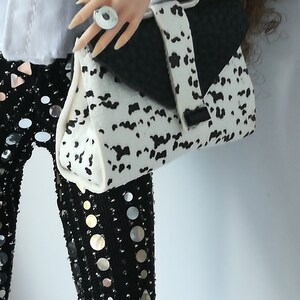 May include: A white and black dalmatian print handbag with a black flap and a silver ring on the handle.