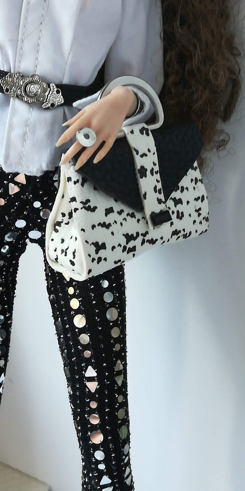 May include: A white and black dalmatian print handbag with a black flap and a silver ring on the handle.