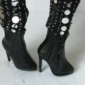 May include: A pair of black heeled boots with a zipper up the back. The boots are decorated with silver sequins and mirrored circles.